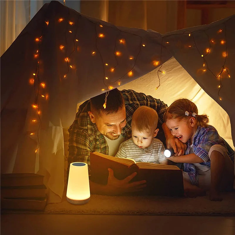 Family enjoying bedtime story with color-changing night light under tent with string lights.